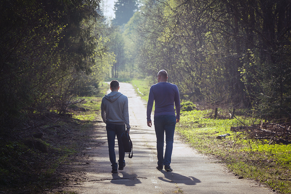 Young man and older man walking side by side in a park