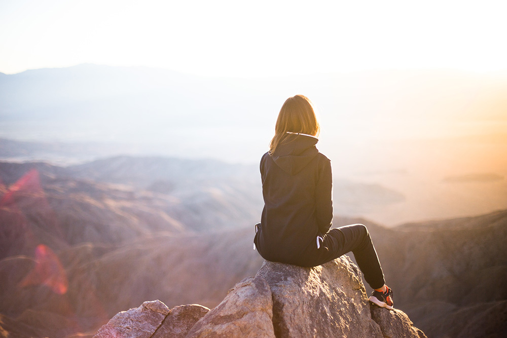 woman sitting on a rock at the top of a hike looking at the sunrise